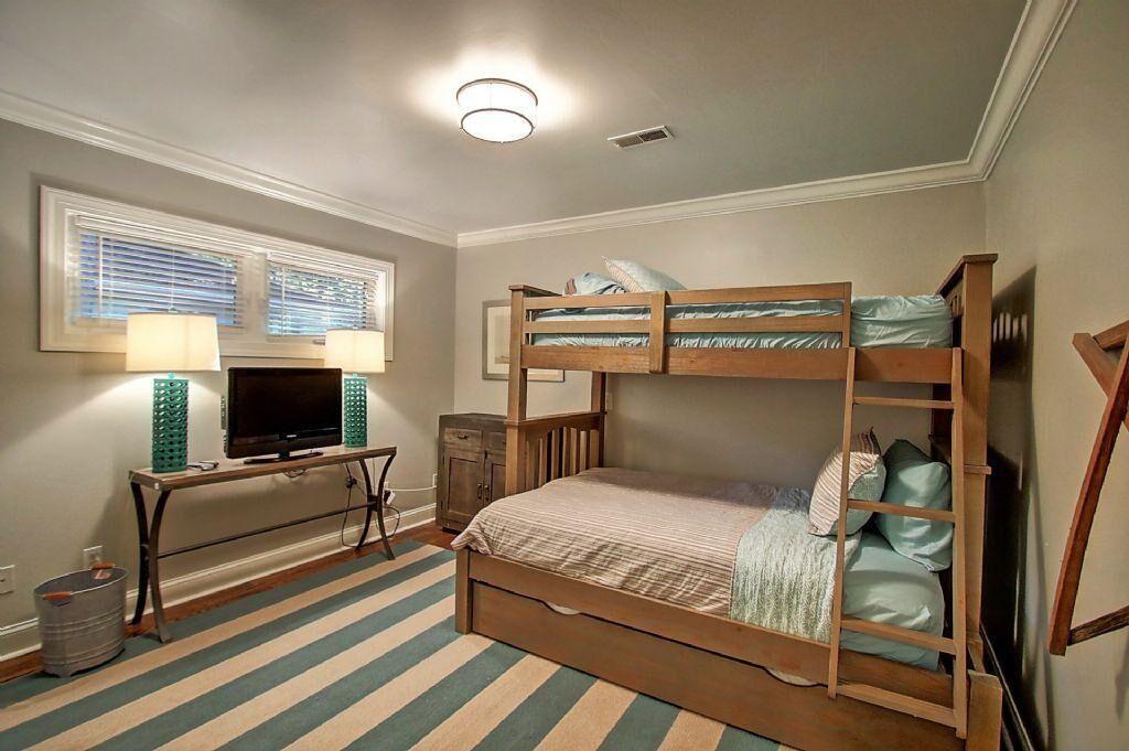 A bunk bed with a TV and desk, a window with blinds, and a striped rug.