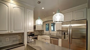 Una cucina moderna con mobili bianchi, elettrodomestici in acciaio inossidabile e illuminazione a sospensione.