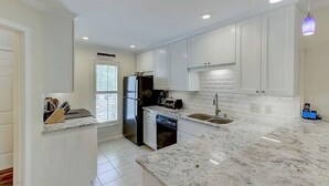A modern kitchen with white cabinets, a black refrigerator, a dishwasher, and a marble countertop. - 50 Fairway Dunes (Isle of Palms)