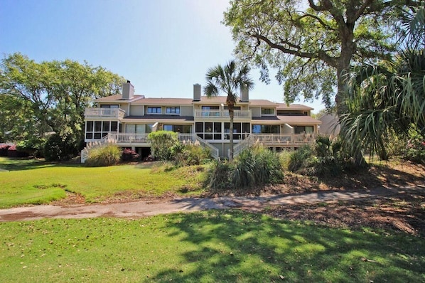 A two-story building with a balcony on the ground floor, surrounded by a well-maintained lawn and trees.