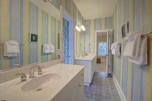 A bathroom with striped wallpaper, a large mirror, a sink, and a shower area.