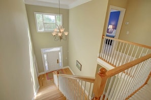 A staircase with white railings and a wooden handrail, leading to a landing with a chandelier and a door.