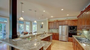 A modern kitchen with granite countertops, stainless steel appliances, wooden cabinets, and pendant lighting.