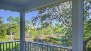 A covered porch with a view of a wooded area and a distant building.