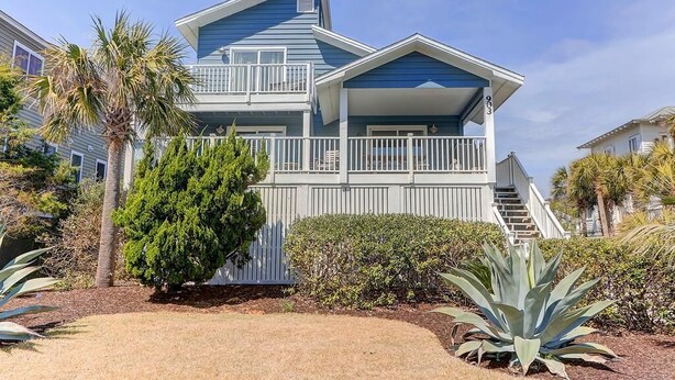 A two-story house with a balcony, surrounded by tropical plants and a well-maintained lawn. - 903 Ocean Boulevard (Isle of Palms)