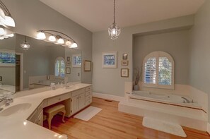 A modern bathroom with a double sink vanity, a large mirror, a chandelier, and a bathtub. - 17 56th Avenue (Isle of Palms)