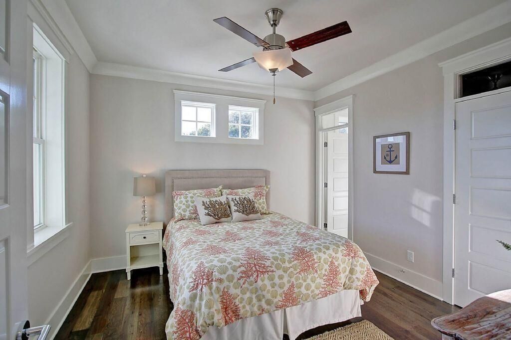 A bedroom with a bed, nightstand, ceiling fan, windows, and a door.