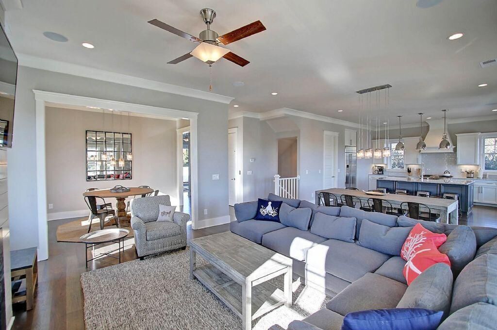 A spacious living room with a large gray sectional sofa, a dining area with a table and chairs, and a kitchen with pendant lights.