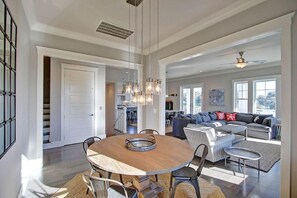 A spacious living area with a round wooden dining table, a gray sofa set, and a kitchen in the background.