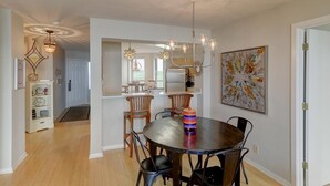 A dining area with a round table, chairs, a chandelier, and a kitchen in the background.