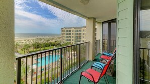 A balcony with a view of a pool and beach, featuring red and blue chairs.