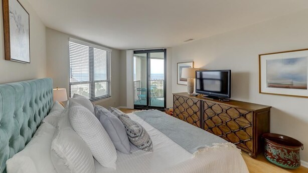 A bedroom with a bed, a television, a dresser, and a balcony door.