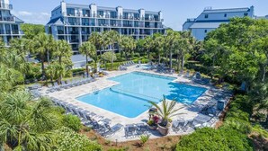 Ett semesterhotell med en central pool omgiven av solstolar och palmer.