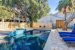 A backyard with a swimming pool, wooden deck, and lounge chairs.