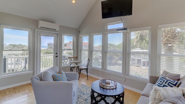 A spacious living room with large windows, a flat-screen TV, and a balcony with a view. - 8 44th Avenue (Isle of Palms)
