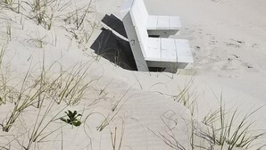 Een zanderig strand met een witte constructie die gedeeltelijk in het zand begraven ligt.