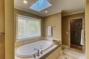 Une salle de bain avec une baignoire sur pieds, une douche à l’italienne, une lucarne et une fenêtre avec des stores.