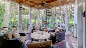 A covered outdoor seating area with wicker furniture, a round table, and a spiral staircase leading to a deck. - 8 Hidden Green (Isle of Palms)