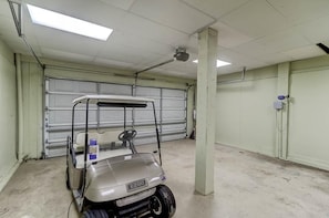 Un parking avec une voiturette de golf au premier plan, une porte de garage fermée à l’arrière-plan et un éclairage fluorescent au plafond.