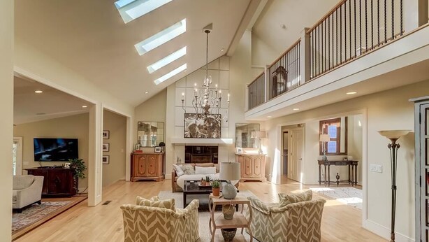 A spacious living area with a high ceiling, a chandelier, and a fireplace. There is a television, a sofa, and a coffee table. - 8 Hidden Green (Isle of Palms)