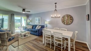 A living room with a blue sofa, white dining table, wicker chairs, and a chandelier. - 101a Oceanside (Isle of Palms)