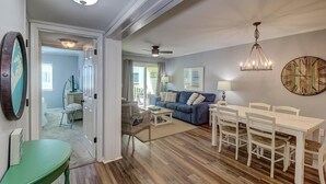 A spacious living room with a blue sofa, white dining table, and a chandelier. - 101a Oceanside (Isle of Palms)