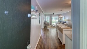 A narrow hallway with wooden flooring, a kitchen area with a counter and sink, and a dining area with chairs and a table. - 101a Oceanside (Isle of Palms)