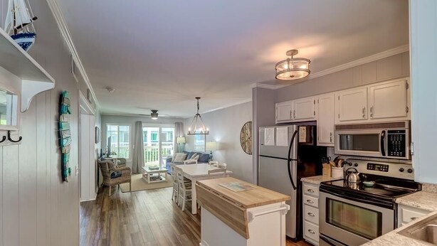 A modern kitchen with white cabinetry, a central island, stainless steel appliances, and a view to the dining area. - 101a Oceanside (Isle of Palms)