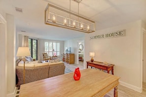 Amplia sala de estar con comedor, un sofá de mimbre, una mesa de madera y un letrero en la pared que dice 'SUMMER HOUSE'.