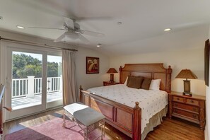 A bedroom with a large bed, two bedside tables, a ceiling fan, and a balcony with a view of greenery. - 2 55th Ave (Isle of Palms)