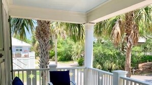 A covered porch with white railings, blue outdoor furniture, and a patterned rug. - 2 55th Ave (Isle of Palms)