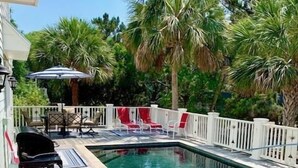 A rectangular swimming pool with a wooden deck, surrounded by palm trees and a white fence. - 2 55th Ave (Isle of Palms)