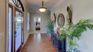 A hallway with wooden flooring, a ceiling light fixture, a large mirror, and a potted plant. - 2 55th Ave (Isle of Palms)