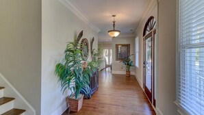 A hallway with wooden flooring, potted plants, a chandelier, and a door with glass panels. - 2 55th Ave (Isle of Palms)