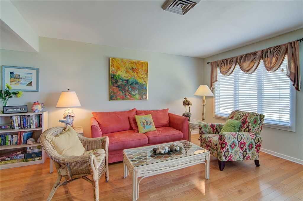 A living room with a red sofa, a glass coffee table, wicker chairs, and a bookshelf.