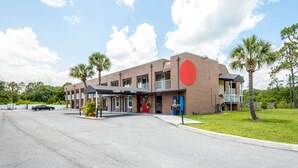 A hotel with a large red circle logo, a covered entrance, and a parking lot. - RW Hotel (Kissimmee)