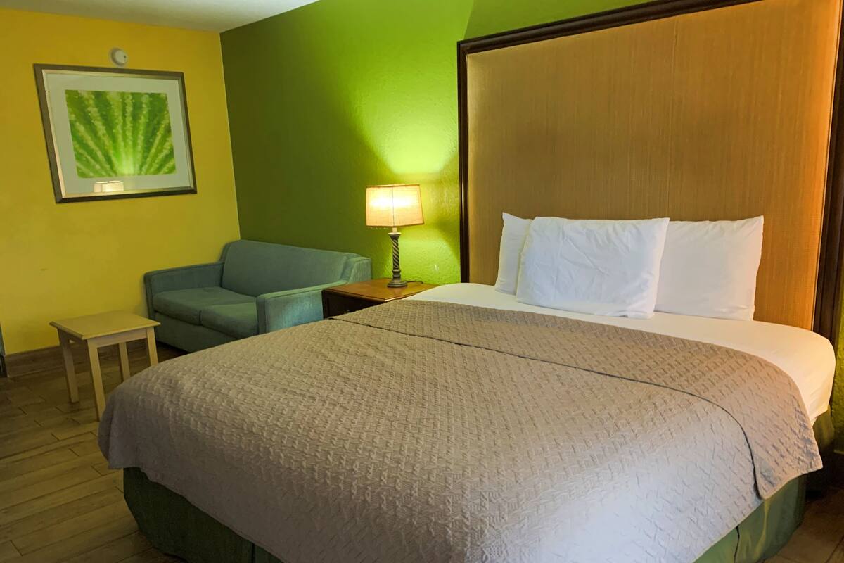 A hotel room with a large bed, a small table, a chair, a lamp, and a framed picture on the wall.