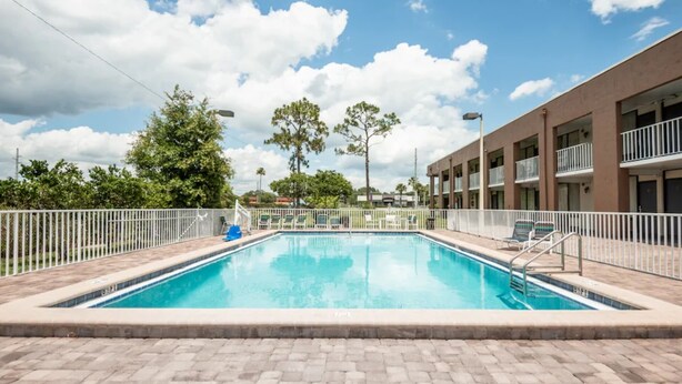 A rectangular swimming pool with a tiled deck, surrounded by a white fence. - RW Hotel (Kissimmee)