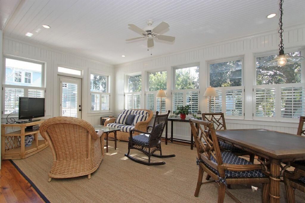 A spacious room with a ceiling fan, large windows with shutters, wicker furniture, and a dining table.
