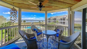 A covered outdoor balcony with wicker furniture and a view of the ocean and buildings. - H303 Tidewater (Isle of Palms)