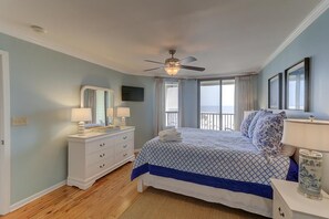 Een slaapkamer met een bed, een dressoir, een plafondventilator, een televisie en een raam met uitzicht.