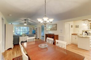 A spacious dining area with a wooden table and white chairs, a chandelier, and a view into the kitchen area with white cabinetry and a countertop. - 22 Twin Oaks (Isle of Palms)