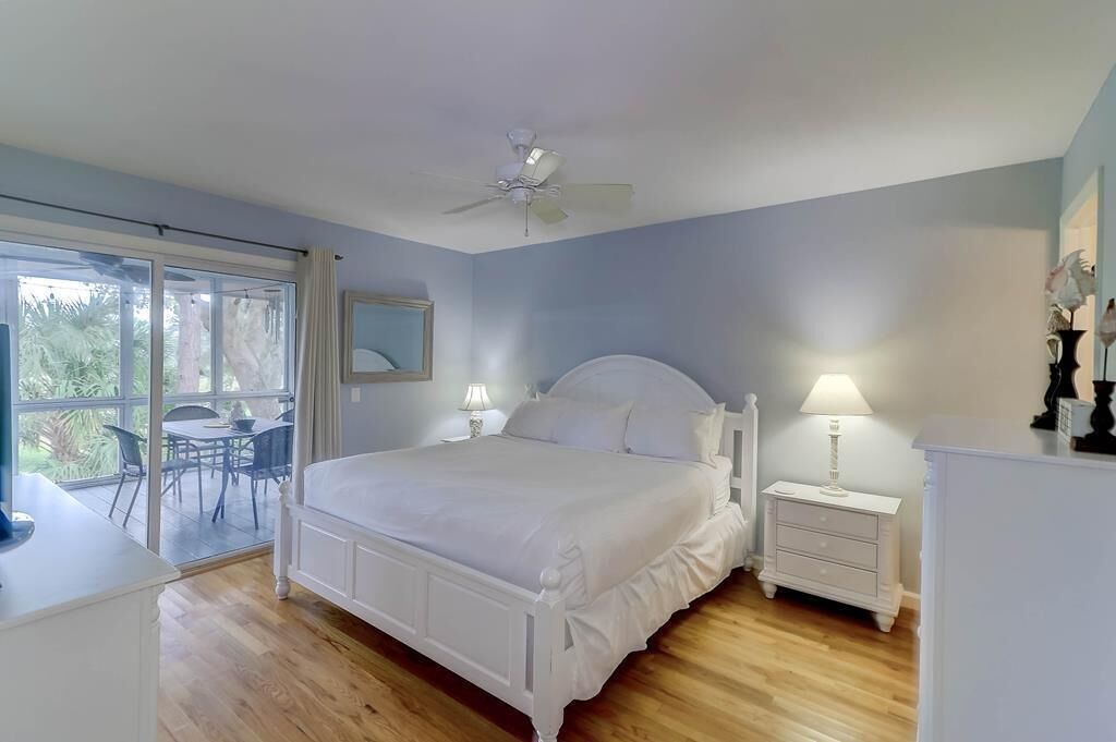 Une chambre dotée d’un grand lit, d’un ventilateur de plafond, d’une table de chevet, d’une commode et d’une porte-fenêtre coulissante donnant sur un balcon.
