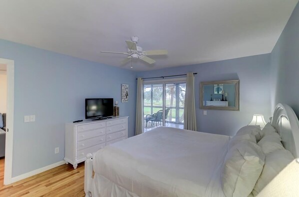 A bedroom with a bed, a television on a dresser, a ceiling fan, and a window with a view of the outdoors. - 22 Twin Oaks (Isle of Palms)