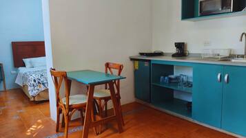 Een knus kamertje met een bed, een eettafeltje met stoelen, een kitchenette met een magnetron en een wastafel.