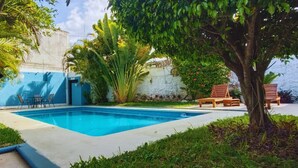 A swimming pool with a blue border, surrounded by greenery and a white wall. - Suites del Sureste (Mérida)