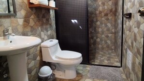 A bathroom with a white sink, toilet, and shower area. There are shelves with towels and a mirror on the wall. - Suites del Sureste (Mérida)