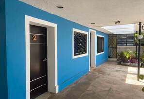 A hallway with blue walls, a door marked with the number 2, and a window with a metal grille. - Suites del Sureste (Mérida)