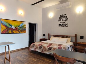 A hotel room with a bed, a desk, a chair, a painting, and a wall with a motivational quote. - Suites del Sureste (Mérida)