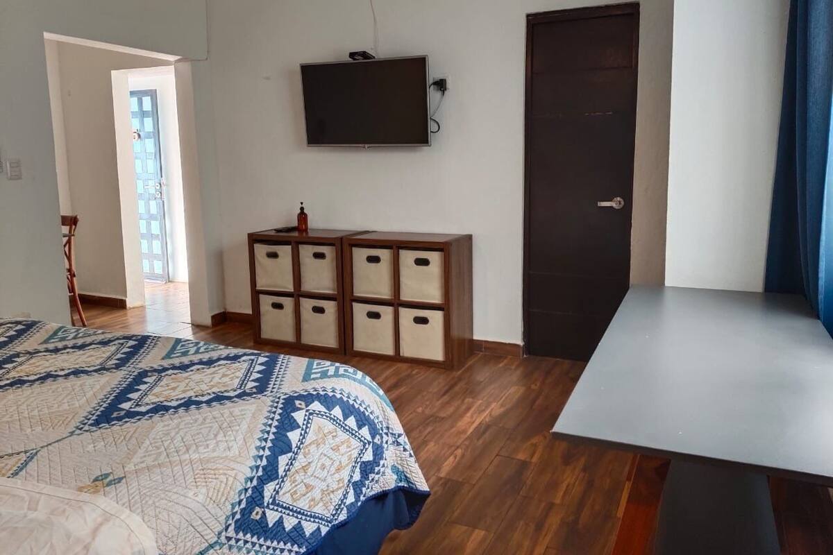 A bedroom with a bed, a TV mounted on the wall, a wooden cabinet, and a door.